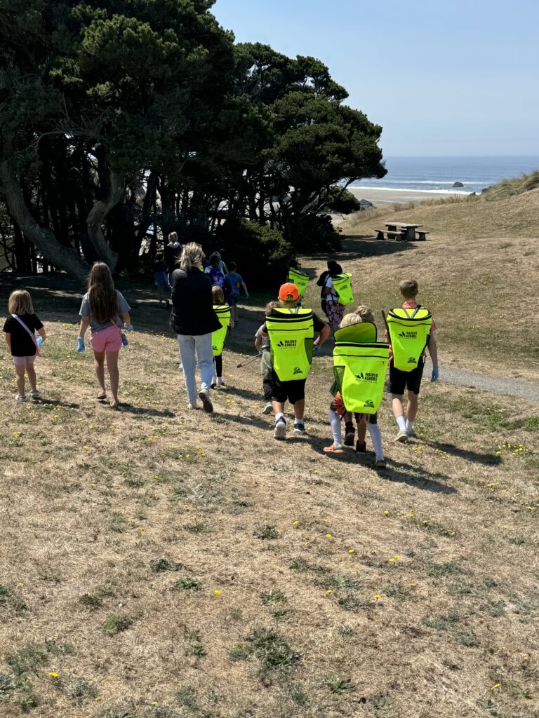 Children wearing high vis yellow backpacks walk towards the beach for a clean up day